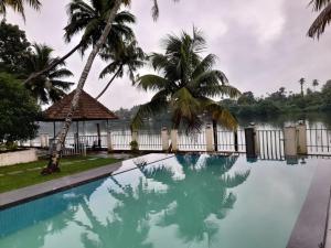 a swimming pool with palm trees and a body of water at RiverSoul Pool Villa in North Paravur