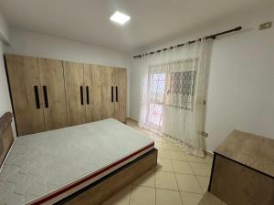 a bedroom with a bed and wooden cabinets and a window at Bledis Apartments in Lushnjë