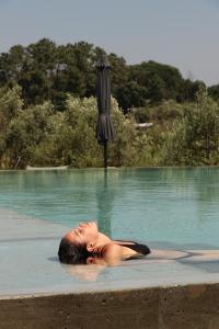 a woman laying in a swimming pool next to an umbrella at Puro Dão Hotel & Spa in Nelas