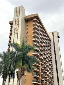 a tall building with a palm tree in front of it at Flat Particular Hotel Kubitschek in Brasília
