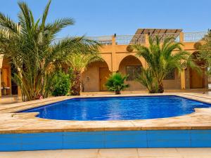 a swimming pool in front of a house with palm trees at Riad Akabar Merzouga in Merzouga