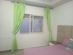 a bedroom with a bed and a window with green curtains at Studio en rez-de-chaussée in Hammamet