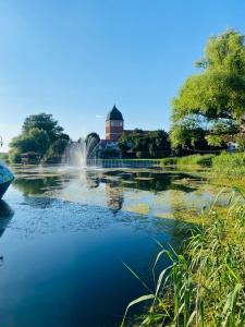 a pond with a fountain and a building in the background at W sercu Rynku in Pasym