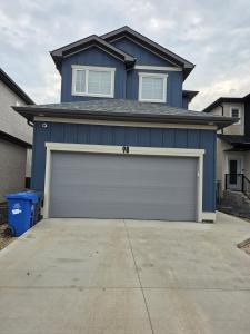 a blue house with a garage door in a driveway at Ope suites Winnipeg in Winnipeg