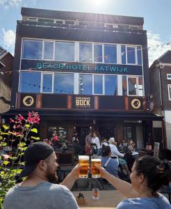two people holding up glasses of beer in front of a brewery at Beach Hotel Katwijk in Katwijk
