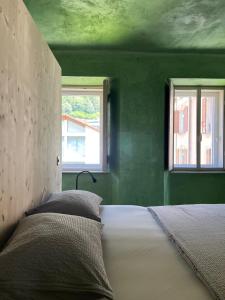a bed in a green room with two windows at Casa Piumogna in Faido