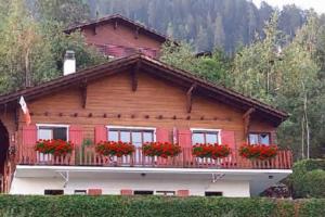 a wooden house with red flowers on a balcony at Havre de paix avec jacuzzi in Grône