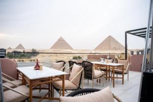 a patio with tables and chairs with pyramids in the background at Le Pacha Pyramids Hotel in Cairo