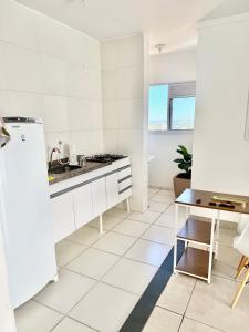 a white kitchen with a refrigerator and a table at Lumar Apart Boituva Diária 24H in Boituva