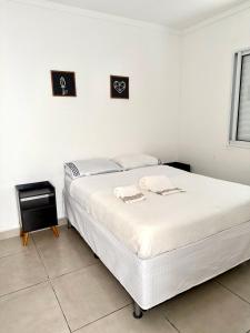 a white bedroom with a bed and two pictures on the wall at Lumar Apart Boituva Diária 24H in Boituva