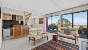 a living room with two chairs and a kitchen with large windows at Nautilus - Modern Lakeside Escape in Lakes Entrance