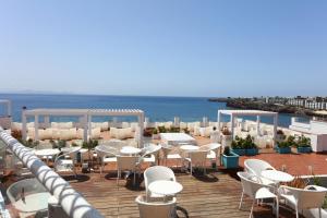 a patio with white tables and chairs and the ocean at Sandos Papagayo in Playa Blanca
