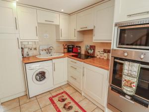 a kitchen with white cabinets and a washer and dryer at Piggery Cottage in Wigton