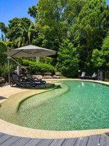 a swimming pool with an umbrella and two chairs in it at Villa Mariposa in Coolum Beach