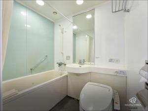 a white bathroom with a toilet and a sink at Daiwa Roynet Hotel Tsukuba in Tsukuba +1 photo