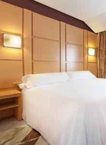 a bedroom with a large white bed and a wooden headboard at Hotel Puertollano in Puertollano