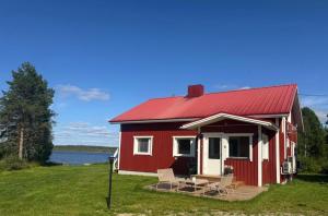 a red cottage with a deck and chairs in front of a lake at Lapland Lakeside Villa in Ranua