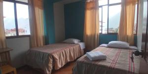 two beds in a room with two windows at Hospedaje Vista Alegre in Oxapampa