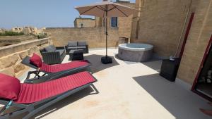 a patio with two chairs and an umbrella and a tub at Razzett Pepprina Poppy Farm in Xagħra