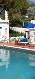 a pool with chairs and umbrellas next to a house at Villa Aida Luxury Apartments & Spa in Forio d'Ischia