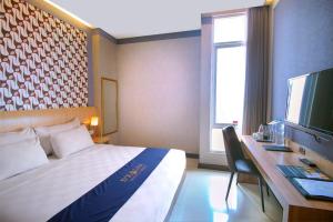 a hotel room with a bed and a desk and a television at D'Kalpa Hotel Demangan Yogyakarta in Yogyakarta