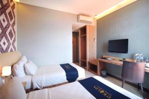 a hotel room with two beds and a desk with a television at D'Kalpa Hotel Demangan Yogyakarta in Yogyakarta