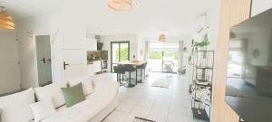 a living room with a white couch and a kitchen at Jolie villa avec piscine chauffée proche du lac in Sanguinet