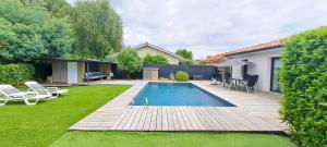 a backyard with a swimming pool and a wooden deck at Jolie villa avec piscine chauffée proche du lac in Sanguinet