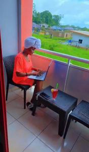 a woman sitting on a balcony using a laptop at Barolena Hotel en appartement in Paramaribo +2 photos