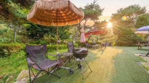 a bbq grill and chairs under an umbrella at Pocheon Arumdri Pension in Pocheon