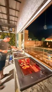 a man standing in a kitchen preparing food on a grill at Pousada Toca do Ceará in Regencia Augusta