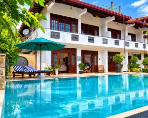 a swimming pool in front of a house with an umbrella at Sky and Sand Guesthouse in Beruwala