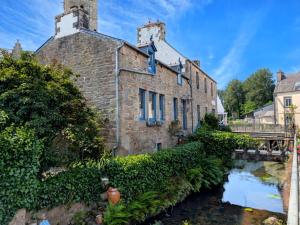 an old brick building with a river in front of it at La Passerelle in Loguivy-Plougras
