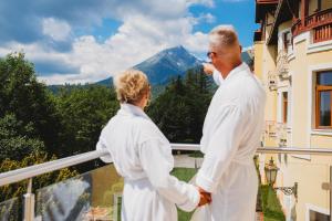 two people standing on a balcony looking at a mountain at Grand Hotel Praha in Tatranská Lomnica
