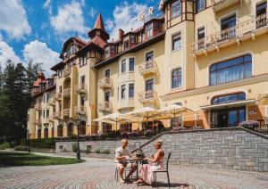 a man and woman sitting on a bench in front of a building at Grand Hotel Praha in Tatranská Lomnica