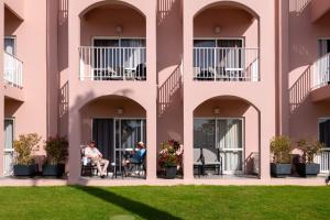 two people sitting on the balcony of a pink building at Vila Gale Collection Praia in Albufeira