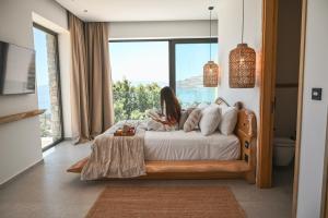 a woman sitting on a bed in a room with a window at Aethra Villa - Infinity Pool & Panoramic Sea View in Pefki +26 photos
