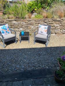two chairs and a table in front of a stone wall at The Threshing Barn Loft in Pont-y-Berem
