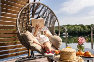 a woman sitting in a wicker chair reading a book at L'Escale Royale Torcy - Marne la Vallée in Torcy