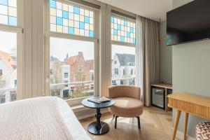 a bedroom with a bed and a chair and windows at City Hotel Rembrandt in Leiden