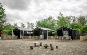 a group of black huts with a bench in a courtyard at Chalet - Camping 't Dekske in Wintelre