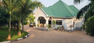 a white house with a green roof and palm trees at COMFORT ZONE Lodge Kigoma in Kigoma