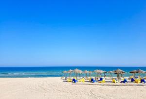 a beach with chairs and umbrellas and the ocean at Yellow Flamingo Studio Fuseta in Fuzeta