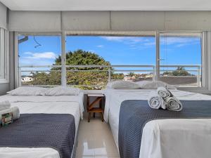 two beds in a room with a large window at AC - Piscina - 1 Suite com banheiro - 200m do mar in Guarujá +15 photos