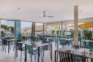 a restaurant with green chairs and tables and windows at Catalonia Ses Estaques - Adults Only in Santa Eularia des Riu