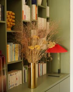 a gold vase with branches in front of a book shelf at MARCELLE EN CAMARGUE - intra muros - piscine et jardin - petit déjeuner compris in Aigues-Mortes