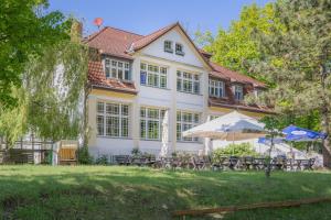 a large white house with tables and umbrellas in front of it at Waldsiedlung Waldhaus App 2.2 in Korswandt