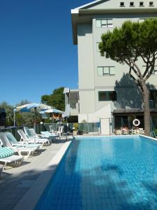 une piscine avec des chaises longues et un bâtiment dans l'établissement Hotel Brasilia, à Lido di Classe