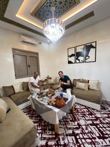 two men sitting in a living room with a table at Merzouga Desert Apartment in Merzouga