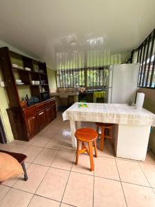 a kitchen with a table and stool and a refrigerator at Casa Colibrí Nature, Pool and Tranquility in Sarapiquí